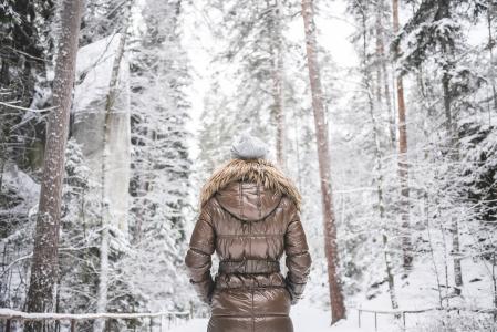 冬天夹克走在多雪的森林里的女孩
